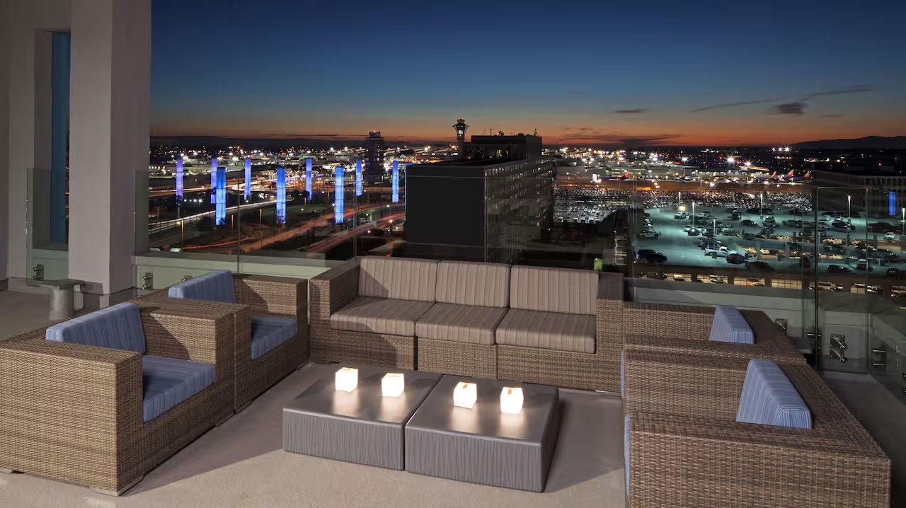 Outdoor lounge furniture on the rooftop pool deck at H Hotel Los Angeles overlooking the LAX skyline at dusk