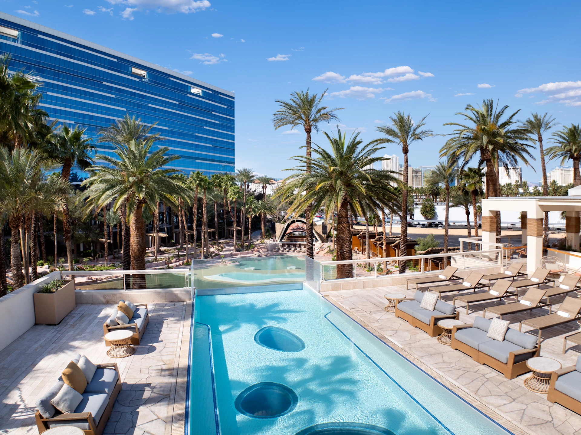 Outdoor pool deck lounge furniture and daybeds at Virgin Hotels Las Vegas with palm trees and city skyline